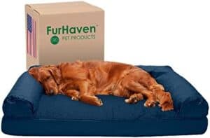 A golden retriever is sleeping on a large, dark blue dog bed. Behind the bed is a cardboard box labeled FurHaven Pet Products with an American flag printed on it.